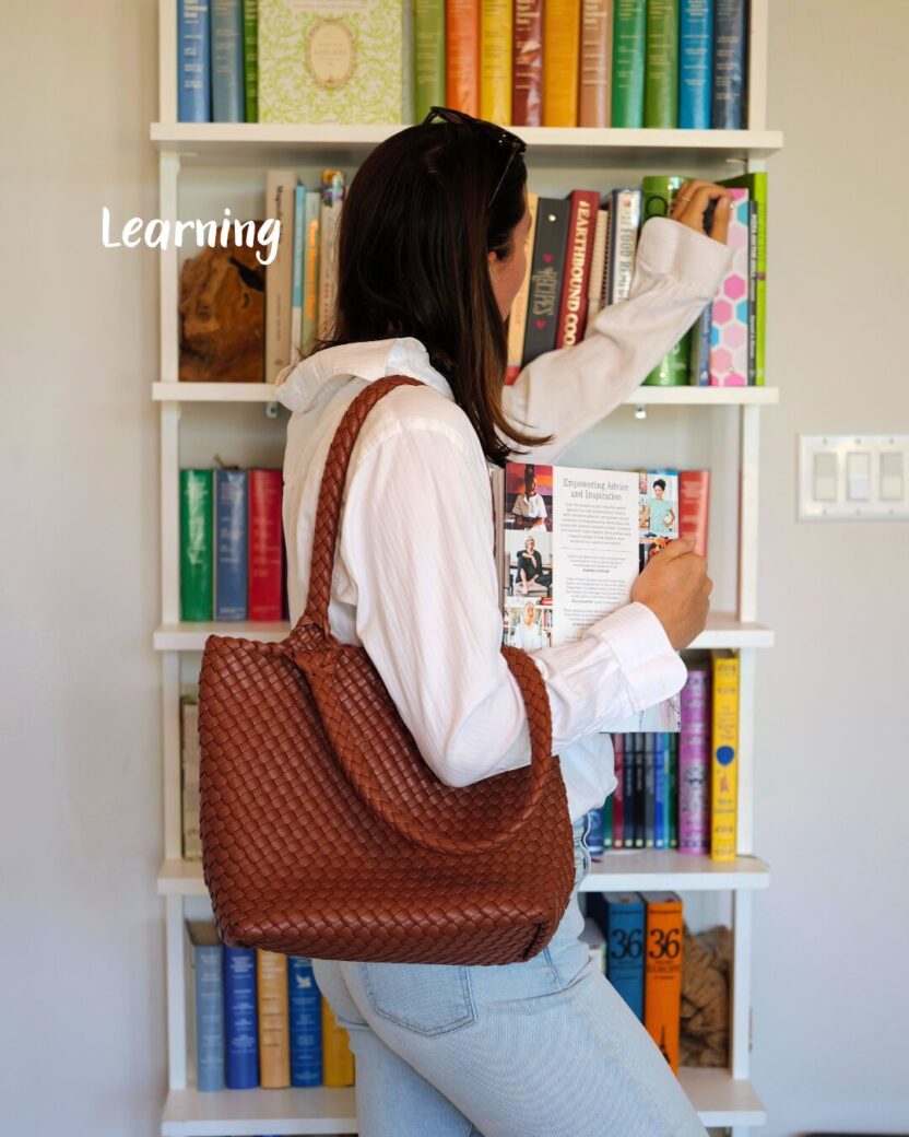 Man in swim trunks holds a baby in a blue life jacket in shallow water.