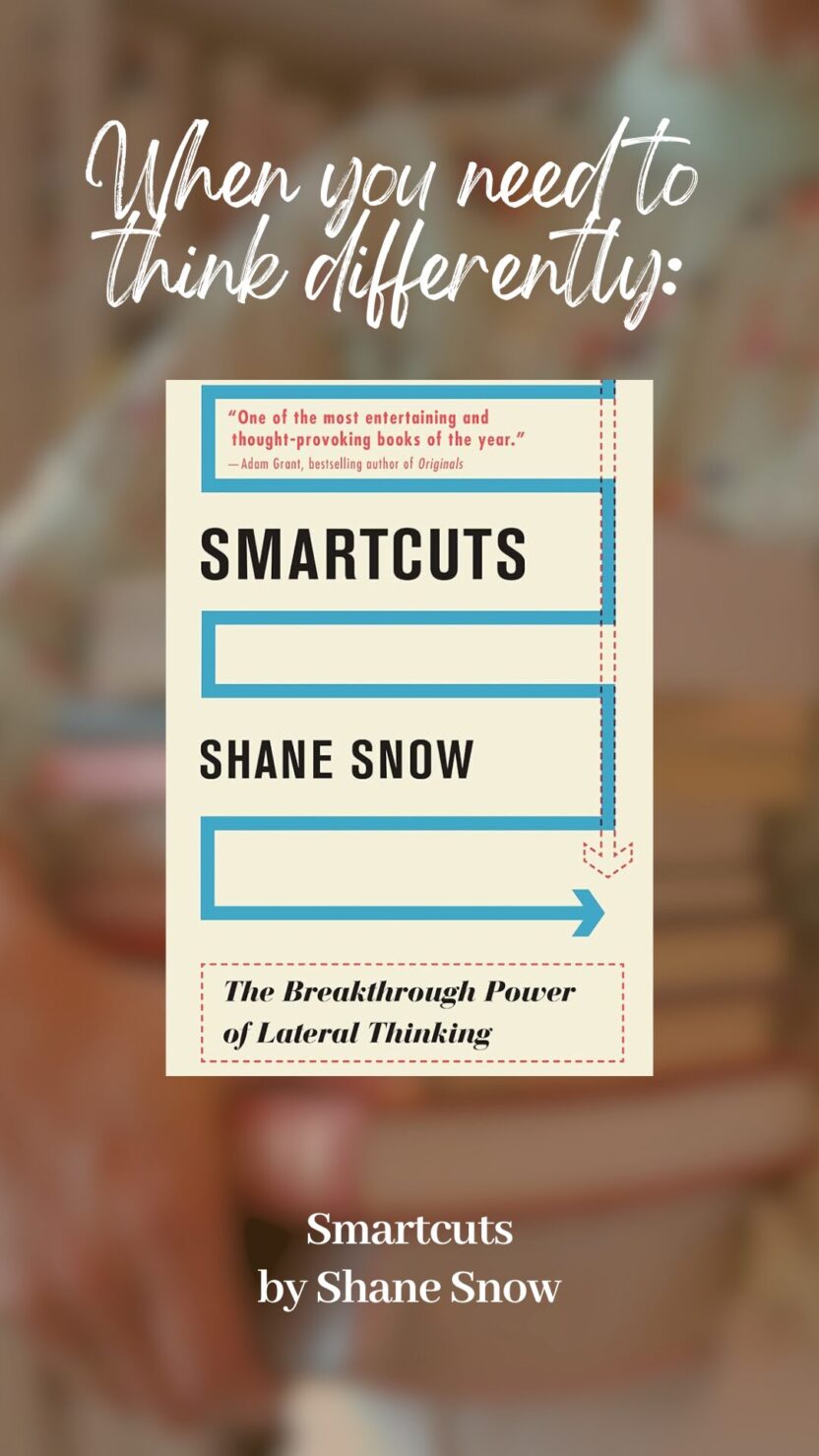 Man in swim trunks holds a baby in a blue life jacket in shallow water.