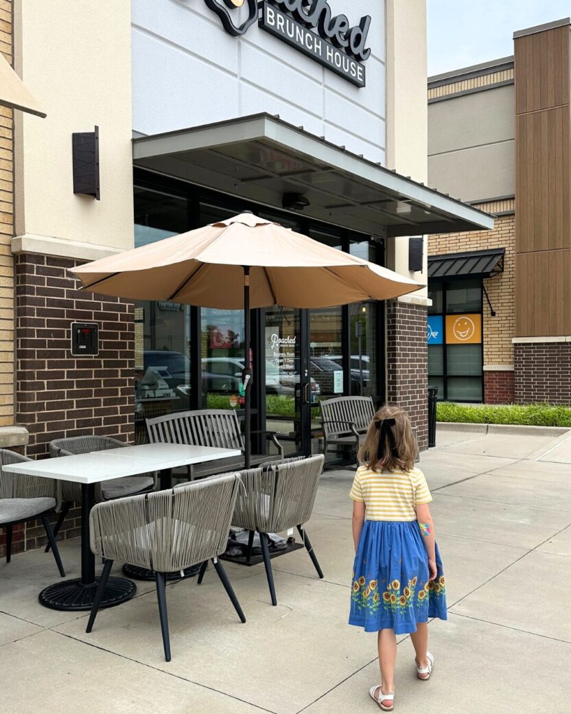 Man in swim trunks holds a baby in a blue life jacket in shallow water.