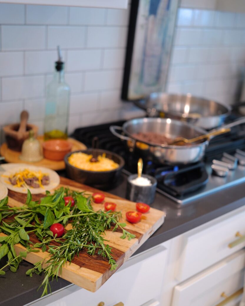 Man in swim trunks holds a baby in a blue life jacket in shallow water.