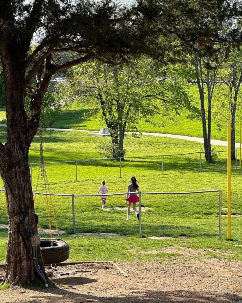 Man in swim trunks holds a baby in a blue life jacket in shallow water.