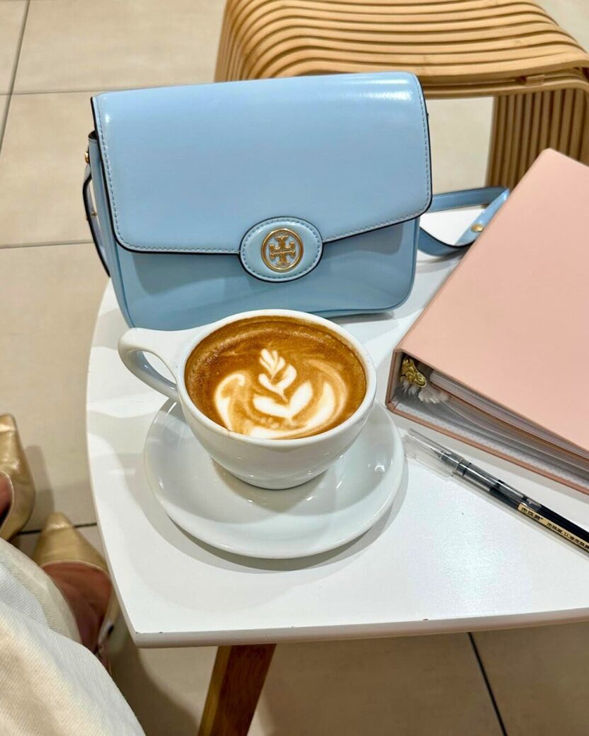 Man in swim trunks holds a baby in a blue life jacket in shallow water.