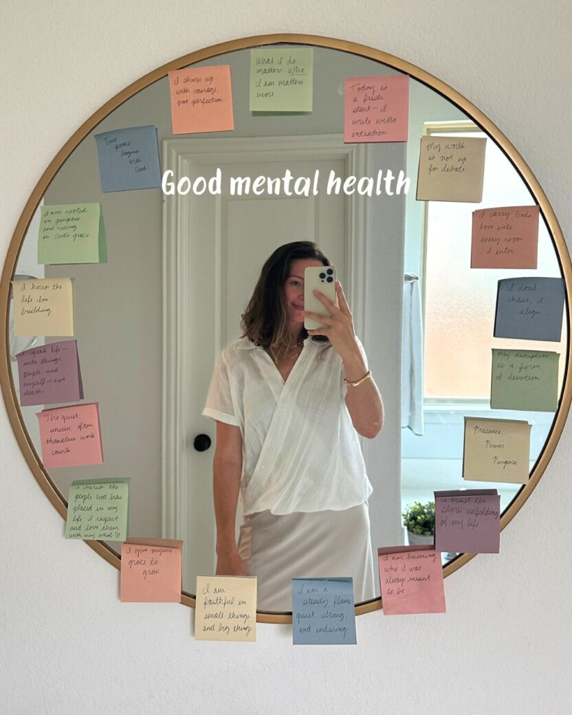 Man in swim trunks holds a baby in a blue life jacket in shallow water.