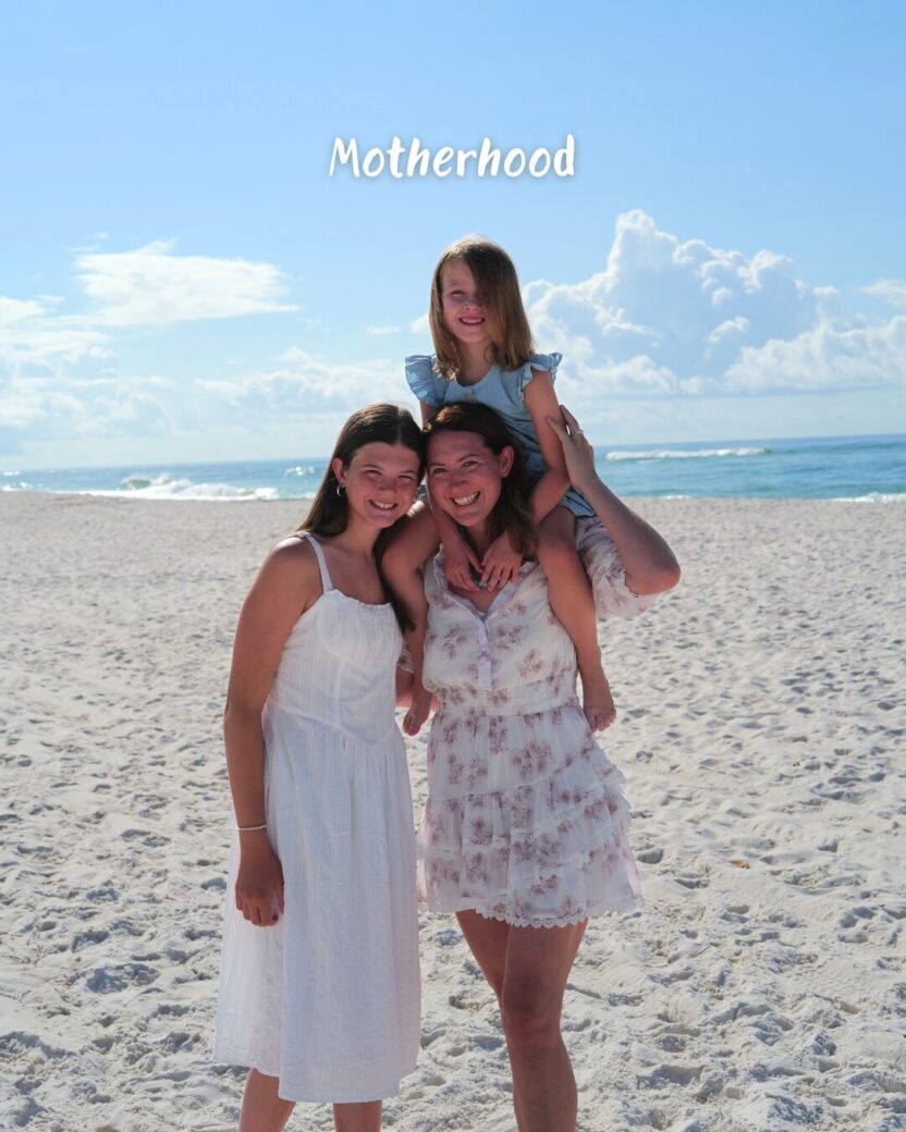 Man in swim trunks holds a baby in a blue life jacket in shallow water.