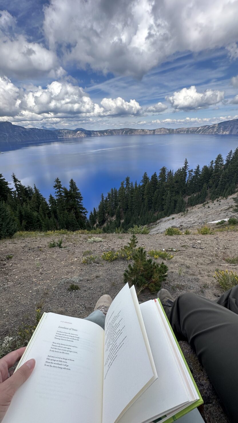 Man in swim trunks holds a baby in a blue life jacket in shallow water.