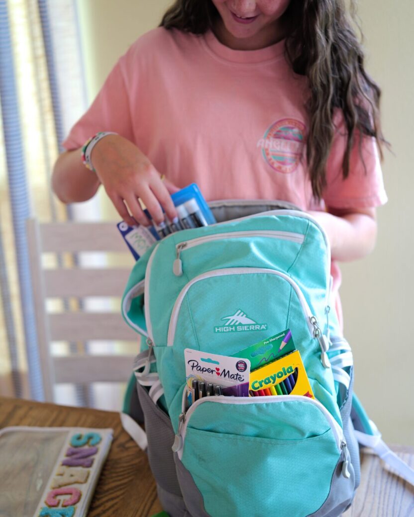 Man in swim trunks holds a baby in a blue life jacket in shallow water.