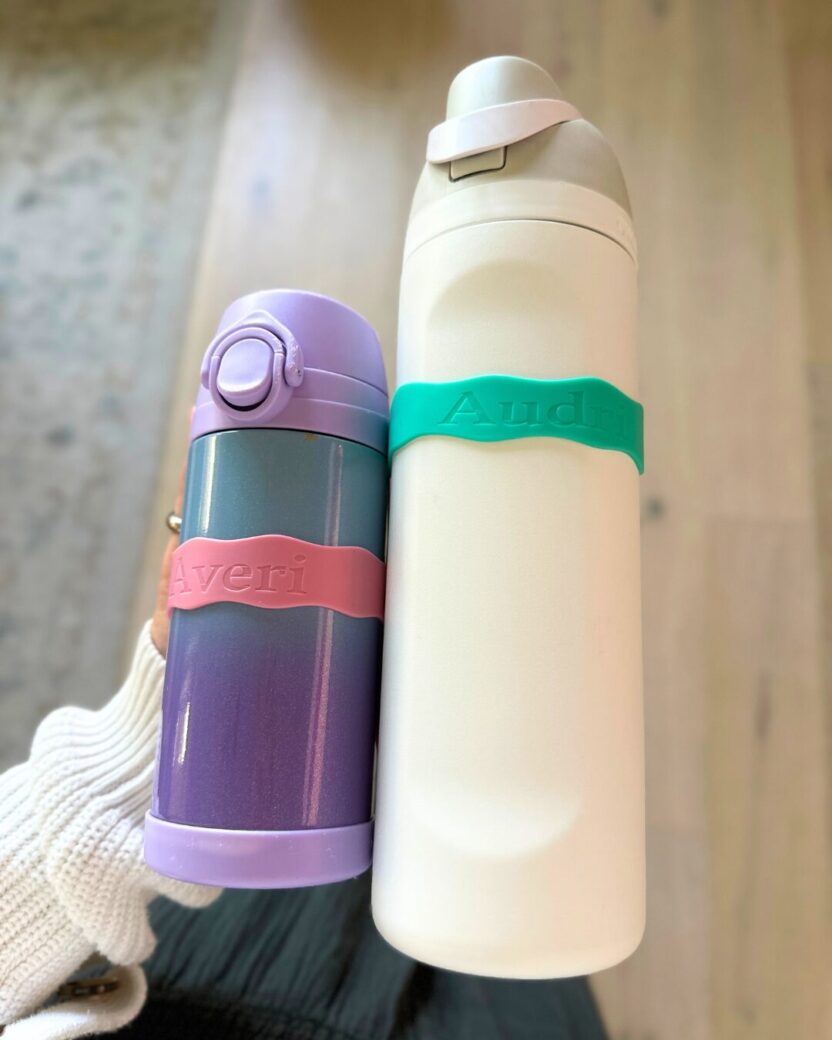 Man in swim trunks holds a baby in a blue life jacket in shallow water.