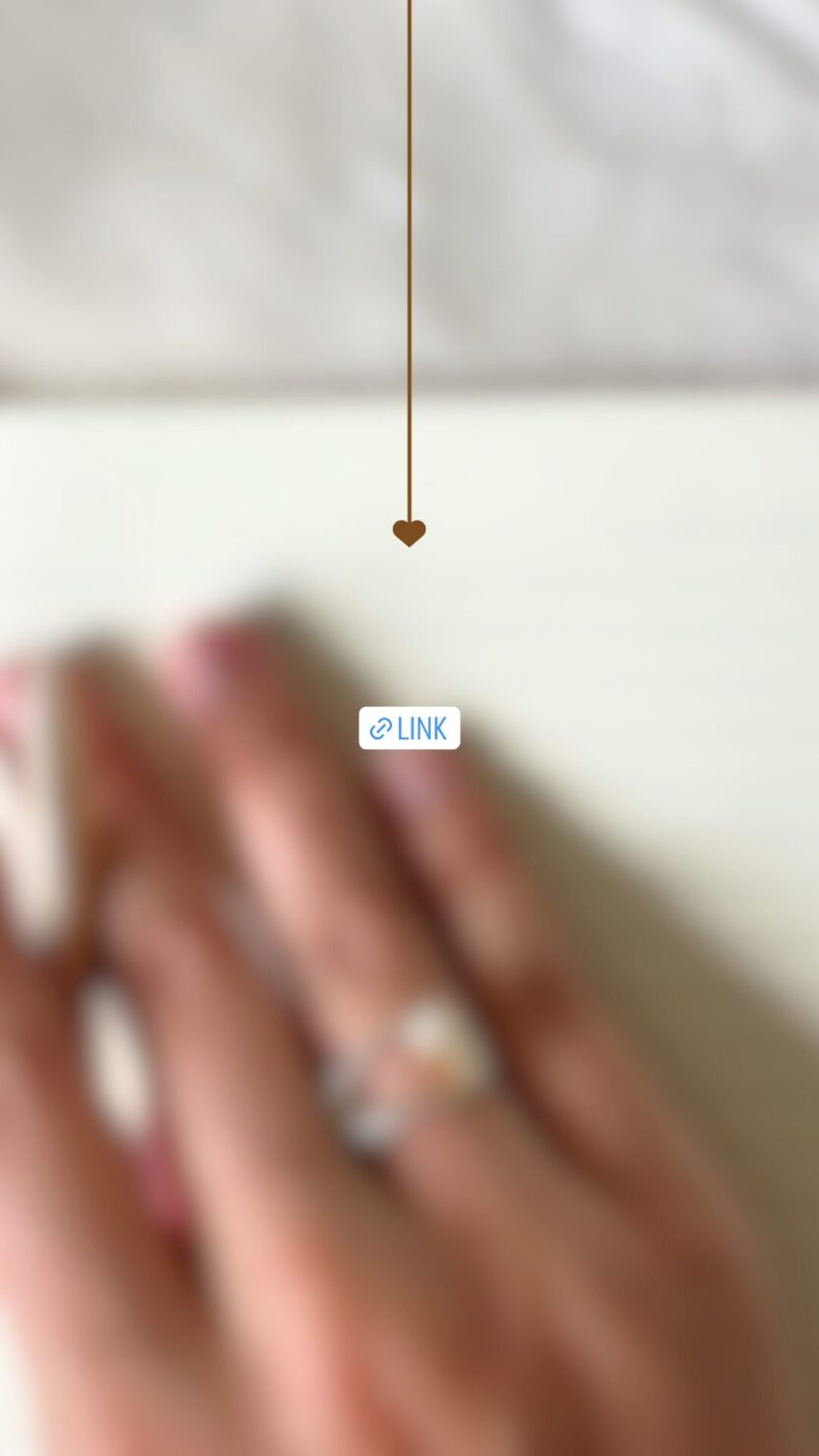 Man in swim trunks holds a baby in a blue life jacket in shallow water.