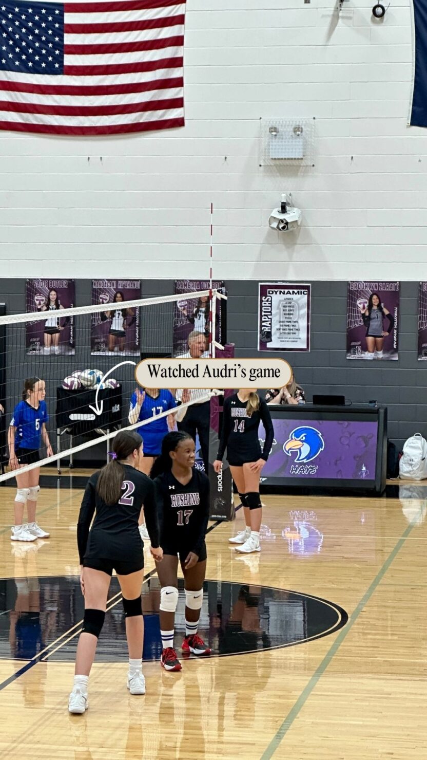 Man in swim trunks holds a baby in a blue life jacket in shallow water.