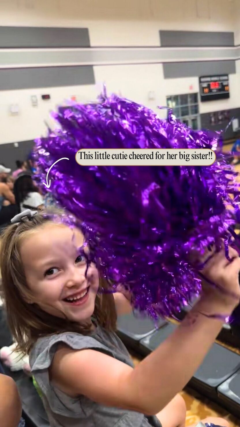 Man in swim trunks holds a baby in a blue life jacket in shallow water.