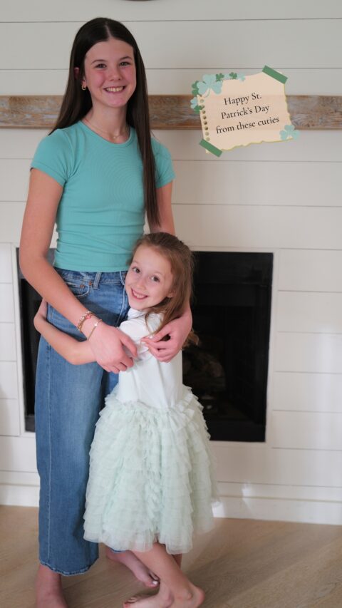 teen girl and little sister smiling and hugging both wearing green for st. Patrick's day