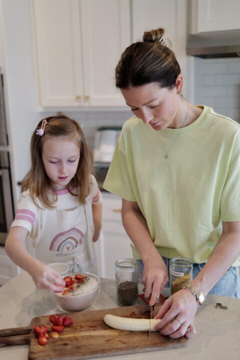 mother and daughter in kitchen chopping fruit and making a protein smoothie bowl