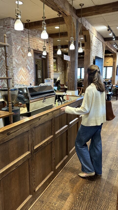 Woman standing at a rustic coffee counter.