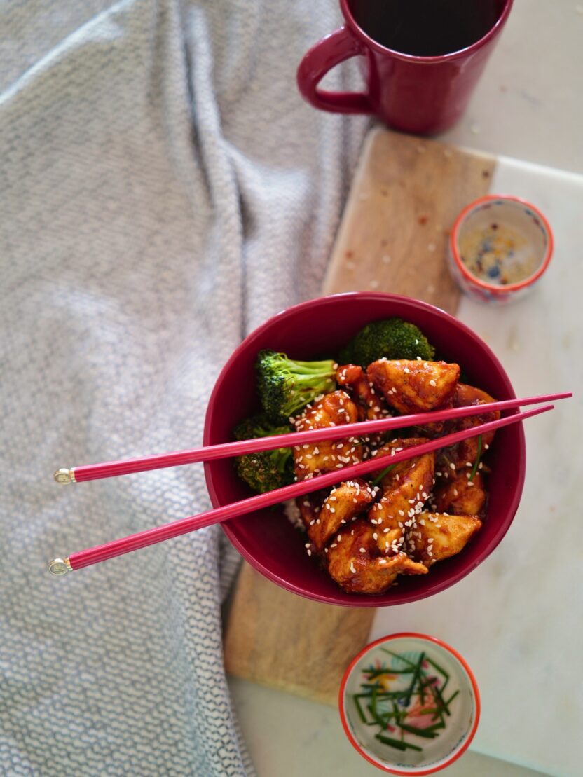 honey garlic chicken and broccoli in a red bowl with chopsticks on a kitchen counter